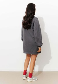 Robe-sweat grise à manches longues, avec des poignets côtelés et une coupe décontractée. Portée avec des chaussettes rouges et des baskets argentées. Design simple, sans motifs.