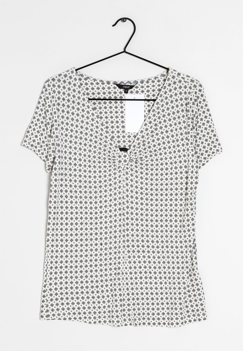 Blusa a maniche corte con scollatura a V, con motivo floreale nero su sfondo bianco, dotata di bottoni frontali e realizzata in un tessuto leggero e morbido.