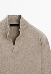 Beige strikket sweater med en ribbet høj krave og en kort V-formet åbning foran, mærket siger Massimo Dutti.