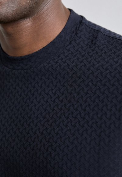 Σκοτεινό ναυτικ�ό μπλουζάκι κοντού μανικιού με υφή από υφασμένο μοτίβο. Στρογγυλή λαιμόκοψη με απλή υφή και χωρίς ορατά μεταλλικά στοιχεία.