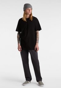 Czarny, oversize t-shirt z miękkiego materiału, z krótkim rękawem, połączony z ciemnoszarymi spodniami. Obuwie w czarno-białą kratę.