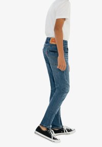Jeans de mezclilla azules con corte recto, cintura a media altura y bolsillos traseros. Combinados con zapatillas de lona negras y una camiseta blanca.