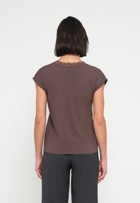 Top marrón de manga corta con un borde de encaje festoneado alrededor del escote, hecho de un material suave. La parte trasera tiene un acabado liso.