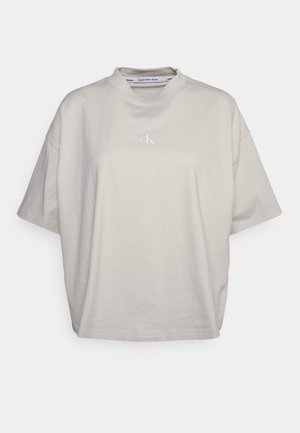 Beige oversized T-shirt met korte mouwen, opstaande kraag en klein wit "cK" logo in het midden van de borst.