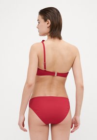 Rød bikini-sett med enkelt design, justerbare stropper og klipslukking. Glatt stoff med matt tekstur og uten mønstre.