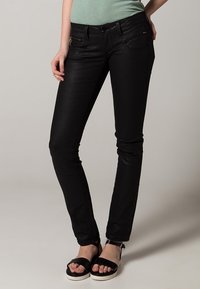 Jeans skinny negros de mezclilla con bolsillos frontales, un detalle de bolsillo con cremallera y un ligero brillo. Combinados con sandalias negras y una blusa verde menta.