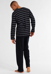 Chemise à rayures marines à manches longues avec des rayures blanches, associée à un pantalon uni marine. Mélange de coton, coupe décontractée, couture visible et sans motifs sur le pantalon.