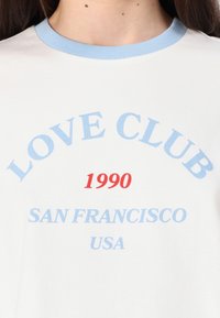 Balta trumpa rankovėmis marškinėliai su šviesiai mėlynu raštuotu apykaklės kraštu. Puikuojasi mėlynu „LOVE CLUB“ ir „SAN FRANCISCO USA“ tekstu, su raudonu „1990“ akcentu.