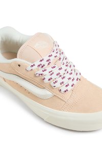 Sneaker en daim pêche clair avec des accents en cuir blanc. Équipé de lacets à motif floral bordeaux et d'une semelle en caoutchouc texturée.