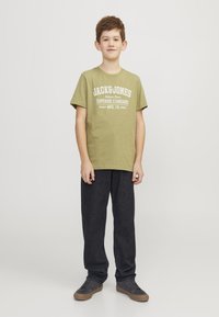 Zelena pamučna majica s bijelim natpisom "JACK & JONES" i "SUPERIOR STANDARD." Uparena s tamnosivim hlačama i sivim tenisicama.