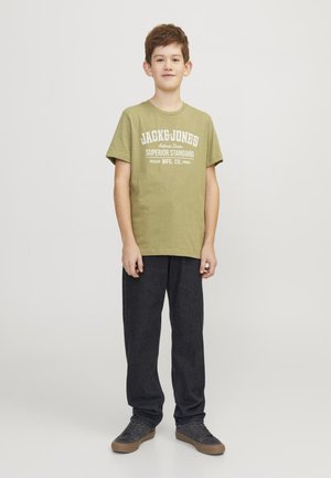 Zeleno bombažno majico z belim napisom "JACK & JONES" in "SUPERIOR STANDARD." V kombinaciji s temno sivo hlačami in sivimi supergami.