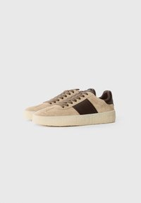 Baskets en daim beige avec des accents en cuir marron, bout rond, semelles texturées et design de bande latérale contrastant. Lacet avec des lacets beiges assortis.