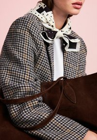 Houndstooth patterned jacket in navy and tan, paired with a black and white polka dot scarf. Brown suede bag with a long strap.