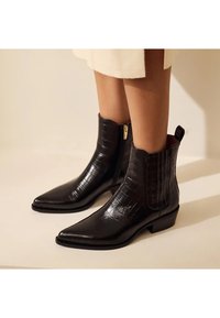Zwarte enkelboots van gestructureerd faux croc leer. Voorzien van een spitse neus, zijrits en een lage blokhak.