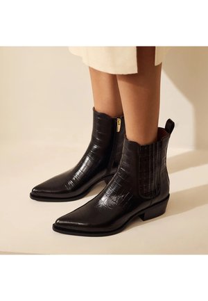 Bottines noires en cuir synthétique texturé effet crocodile. Dotées d'un bout pointu, d'une fermeture zippée sur le côté et d'un petit talon carré.