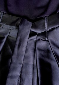 Mörk marinblå plisserad kjol med en bred midjeband och ett matchande knytbälte i ett mjukt, strukturerat tyg.