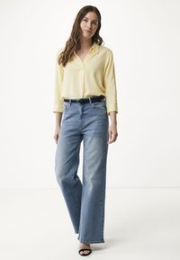 Camicia collared a maniche lunghe di un giallo chiaro abbinata a jeans in denim blu a vita alta. Design a gamba larga con una cintura a pois bianco e nero.