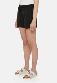 Pantaloni corti neri realizzati in tessuto leggero con un elastico in vita e un cordoncino. Abbinati a sandali bianchi con suola in sughero.