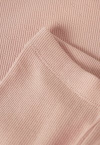 Tejido ribeteado de color rosa claro con pequeños patrones texturizados. Presenta un borde suave con costuras visibles. Primer plano de los pliegues del material.