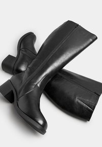 Svarta läderstövlar i knähöjd med en slät yta, med sidodragkedja, blockklack och subtil sömnadsdetaljering längs sömmarna.