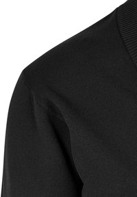 Fekete pulóver részlet, amely texturált kötött anyagból készült, kerek nyakkivágással és bordázott gallérral rendelkezik. A szövet minőségére és sima megjelenésére összpontosít.