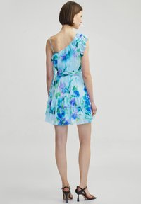 Vestido de gasa con un diseño de un solo hombro, acentos de volantes, falda en capas y un patrón floral azul sobre un fondo claro.