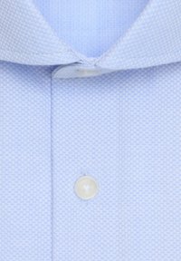 Chemise habillée bleu clair texturée avec un bouton blanc fermé près du col, montrant un gros plan du motif du tissu et des coutures.