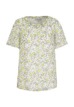 Kvinde iført hvid denimjakke, grøn og hvid blomster-top, olivengrønne bukser og hvide ankelstøvler med chunky hæle.