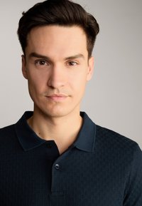 Dunkelblauser Poloshirt mit einem strukturierten geometrischen Muster, mit Kragen und einer Knopfleiste mit zwei Knöpfen. Glatter Stoff, körpernaher Schnitt.