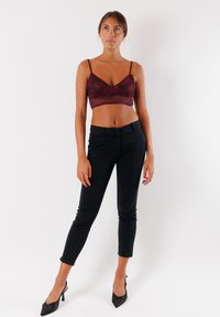 Crop top in pizzo bordeaux con spalline sottili abbinato a jeans skinny neri a vita alta e tacchi neri a punta. Texture dei tessuti liscia.