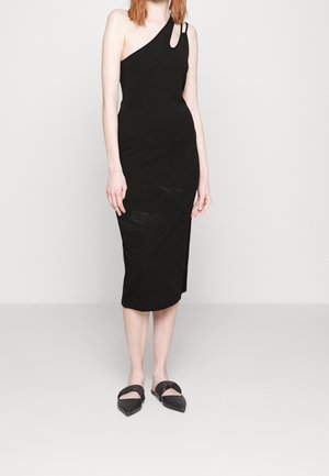 Abito midi nero aderente con design asimmetrico a spalla scoperta, caratterizzato da un taglio e dettagli con elastico. Texture liscia, indossato con mules a punta nera.