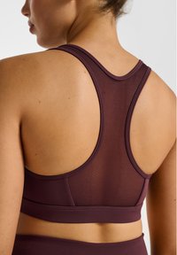 Bordeauxrode sportbeha met racerback-design, voorzien van een mesh paneel voor ademend vermogen en gladde randen voor comfort en ondersteuning.