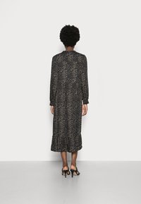 Abito lungo con stampa leopardata nera e beige, caratterizzato da maniche lunghe, orlo arricciato e polsini arricciati, indossato con sandali neri con tacco alto.