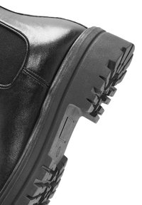 Czarne skórzane buty z teksturowaną gumową podeszwą o wyrazistym wzorze, elastycznymi bokami oraz solidnym projektem obcasa.