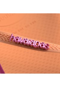 Havaianas natikači imajo teksturiran oranžen trak z roza, izbočeno logo. Podplat je vzorčen za boljši oprijem.