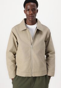 Beige lightweight jacket with a zippered front, large collar, and two side pockets. Fabric appears smooth with a relaxed fit.