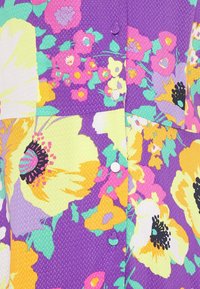 Tessuto a motivi floreali con grandi fiori gialli e viola su uno sfondo viola vibrante. Superficie texture con cuciture visibili.