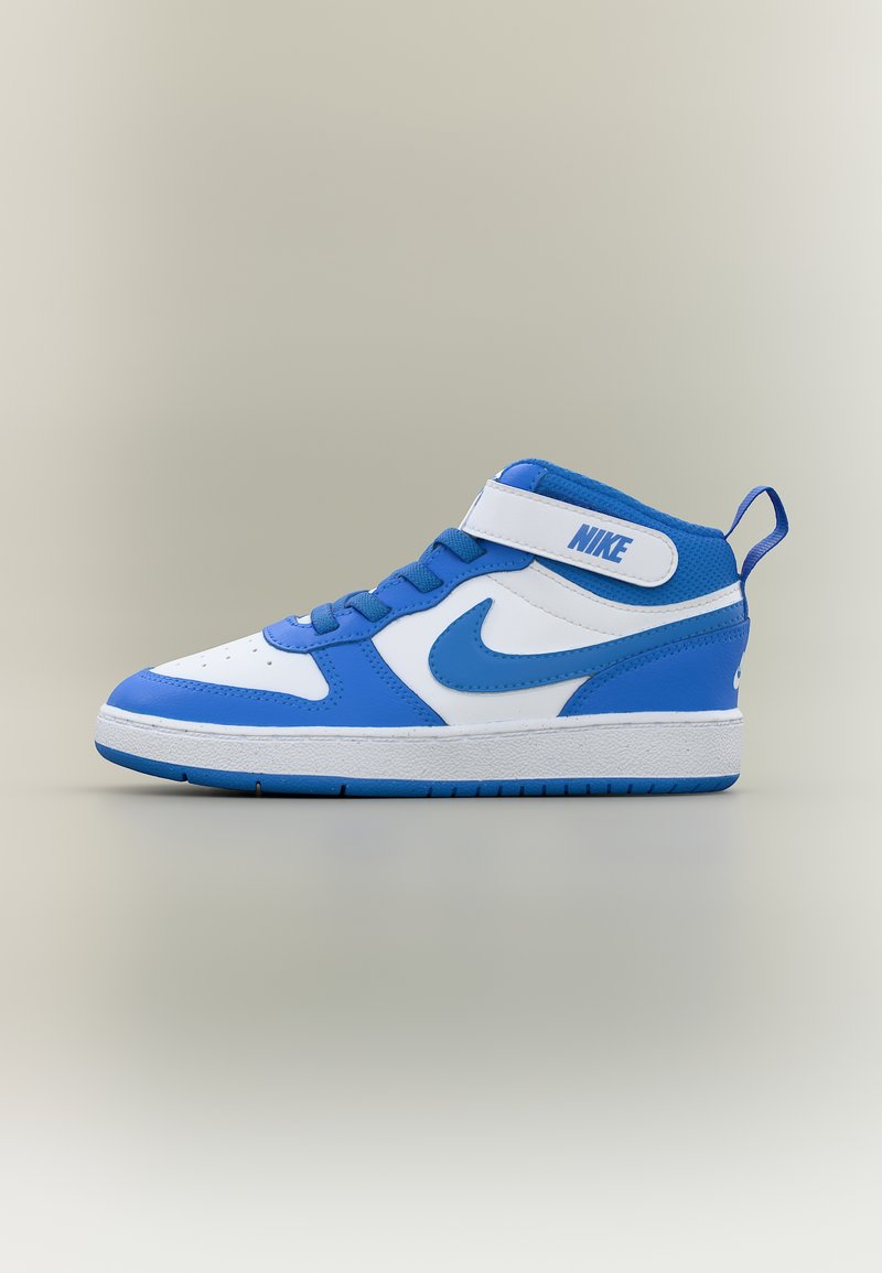 Baskets montantes Nike bleu et blanc avec une bride en Velcro, le logo Nike swoosh sur le côté et une semelle en caoutchouc sur un fond beige uni.