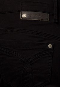Mustat farkut, joissa on nahkainen Calvin Klein Jeans -labeli, erottuva ompelujälki ja metalliset korostukset takataskussa.