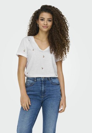 T-shirt en coton blanc à col en V, avec une petite broderie de cerises rouges et vertes, associé à un jean en denim bleu taille haute.