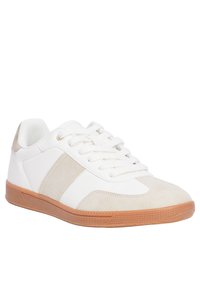 Baskets blanches avec des accents en suède beige, semelle en caoutchouc texturée, bout arrondi et design à lacets. Présente une finition lisse semblable à du cuir.