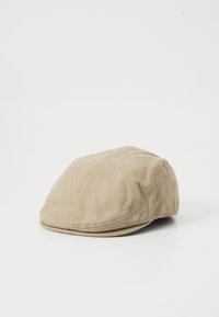 Gorra plana beige hecha de suave tejido de algodón, con forma redondeada, detalles cosidos y una textura lisa.