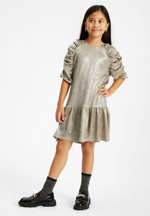 Csillámló ezüst ruha, ráncolt ujjakkal, bővülő szegéllyel és puha textúrával. Fekete platform cipővel és texturált, térd fölé érő zoknikkal párosítva.