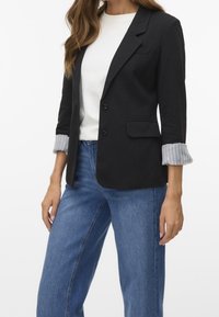 Svart blazer med skräddarsydd design, framknappar och slagkrage. Ärmarna har ett lätt grått randigt tyg. Matchas med blå jeans.