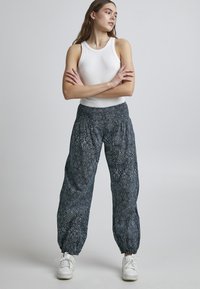 Pantalons amples bleu marine à motif avec une taille élastique et des poignets froncés, associés à un débardeur blanc ajusté et des baskets blanches.
