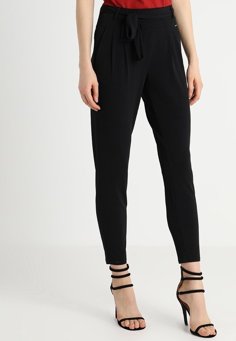 Černé kalhoty na míru s páskem v pase, slim fit a hladkou texturou. V kombinaci s černými sandály na vysokém podpatku s pásky.