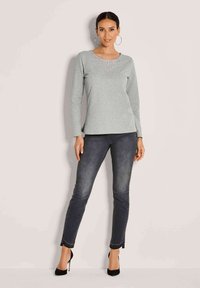 Hellgraues Langarmoberteil mit einem strukturierten, verzierten Rundhalsausschnitt, kombiniert mit dunkelgrauen, schmal geschnittenen Jeans und schwarzen High Heels.