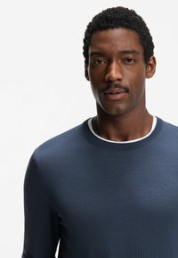 Maglione in maglia blu navy con scollo rotondo e rifiniture bianche a contrasto. Texture liscia con maniche lunghe, design aderente.