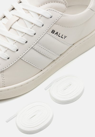 Hvide lædersneakers med tekstureret overflade, vandrette striber og sort branding. To hvide snørebånd er placeret ved siden af skoen.