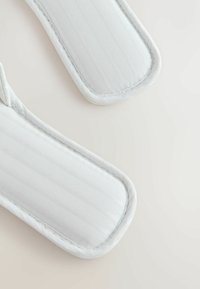 Kaks valget riidest rihma õmmeldud servadega helel pinnal, näidates tekstuuri ja polsterdatud disainielemente.